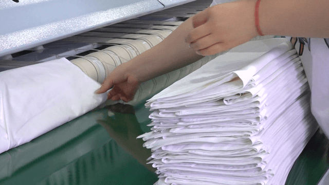 Worker stacking neatly folded sheets in laundry factory