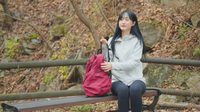 Young woman standing up with backpack on autumn trail bench