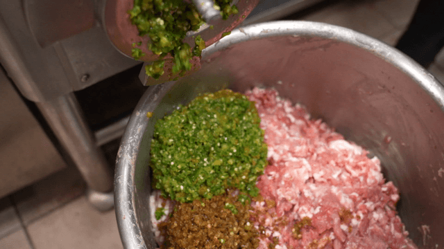 Minced chili falling into container of ground meat from grinder