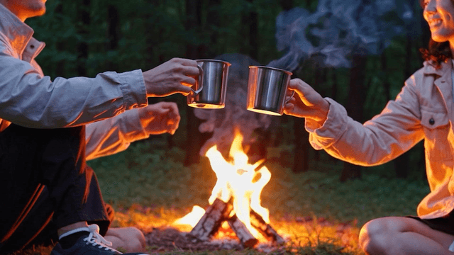 Man and woman clinking glasses in front of a campfire