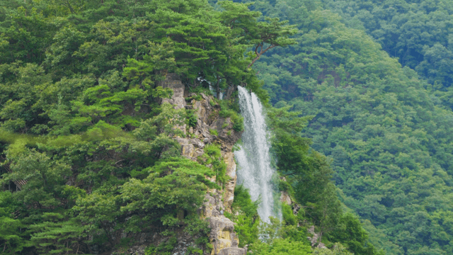 Waterfall flowing along cliff in green mountains