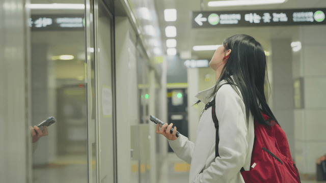Young woman waiting on subway platform while checking phone