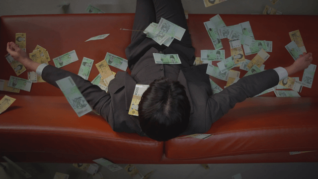 Cash raining down on a man sitting on a sofa