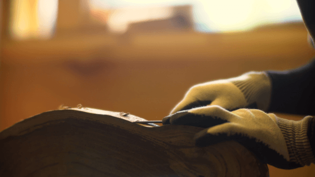 Hands wearing gloves carving wood indoors