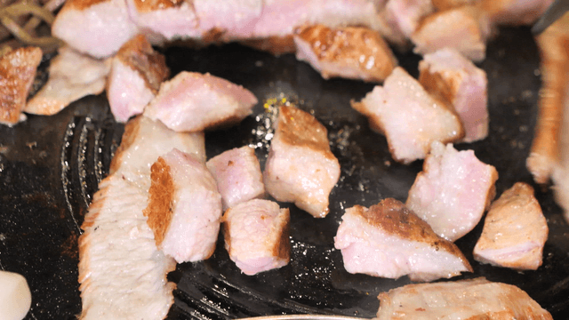 Tongs grilling pork jowls