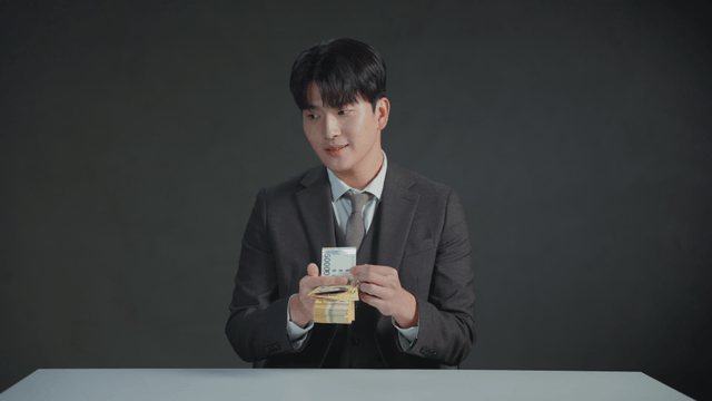 Man in a suit counting money at a desk with a satisfied expression