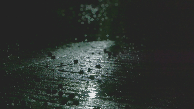 Rain falling on a wet pavement under dim light