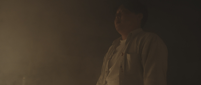 Man with a scarred face standing in a dark place