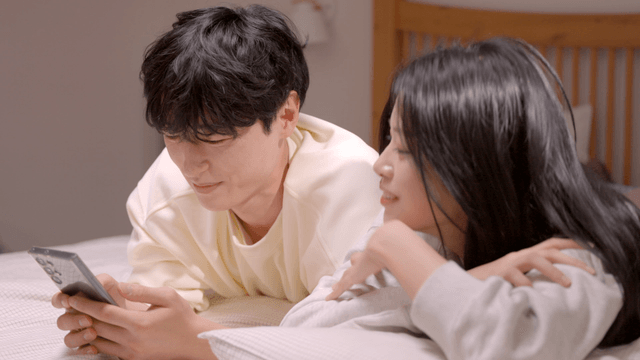 Couple relaxing in bed while looking at smartphone