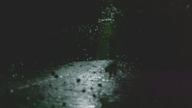Rain falling over a dark street at night