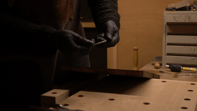 Artisan inserting metal wire into black wooden board