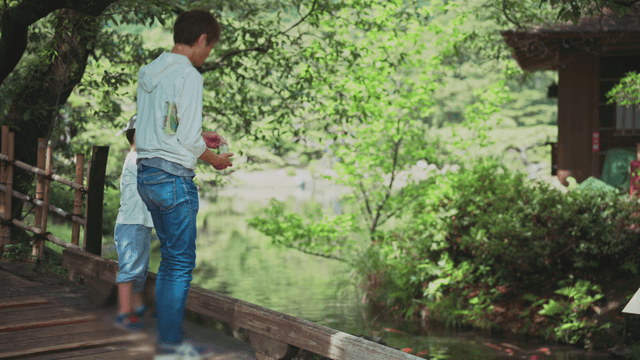 Father and son feeding fish by a pond