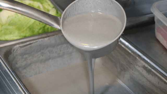 Ladle scooping viscous black bean soy liquid