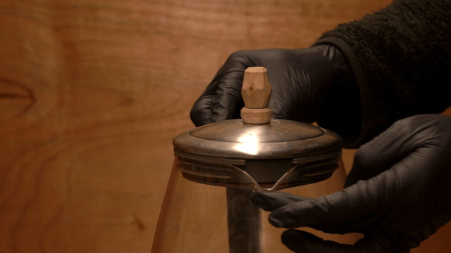 Artisan handling a glass teapot with a handcrafted wooden lid handle
