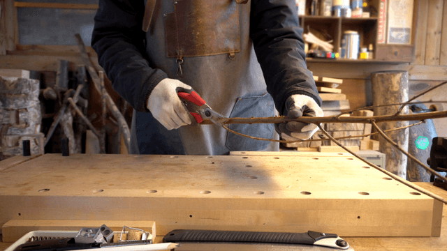 Carpenter trimming wooden branches with shears in workshop