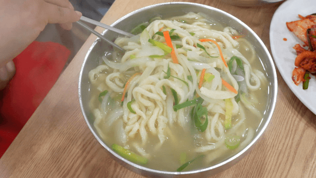 Chopsticks stirring hand-cut noodles with vegetables