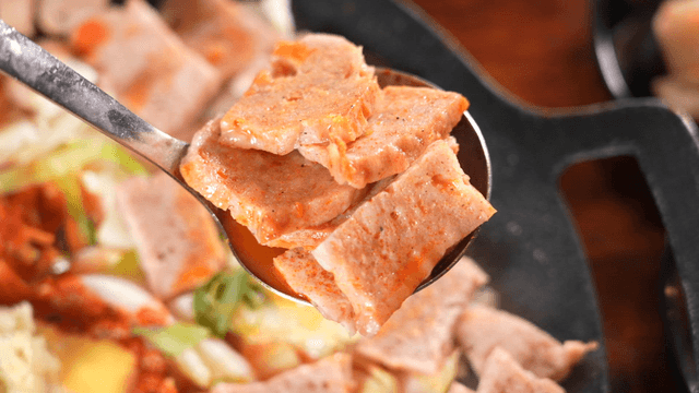 Steaming ladle lifting stir-fried ham pieces