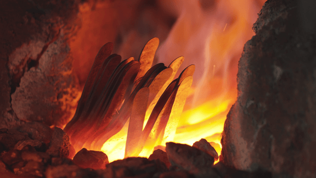 Worker removing heated metal piece from forge