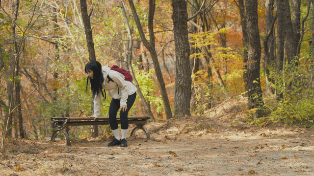 Young woman massaging legs on bench in autumn forest