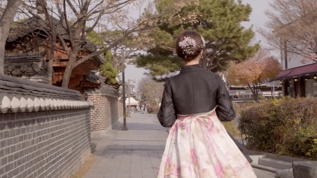 A woman in hanbok walking along a traditional Korean street