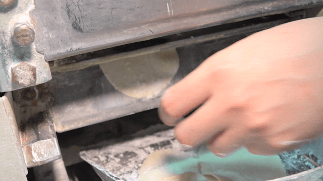 Hand taking dumpling wrappers from a machine