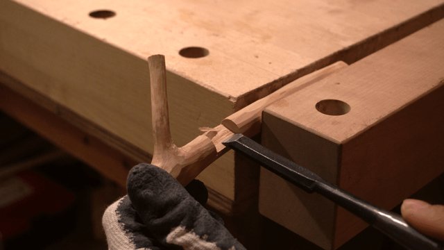 Hands carving wood with a chisel on workbench