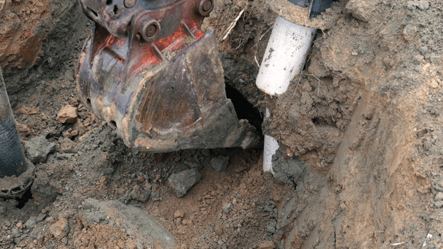 Excavator digging near a pipe in the soil