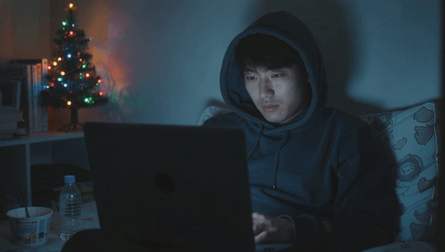 크리스마스 트리가 있는 어두운 방에서 노트북을 사용하는 젊은 남성