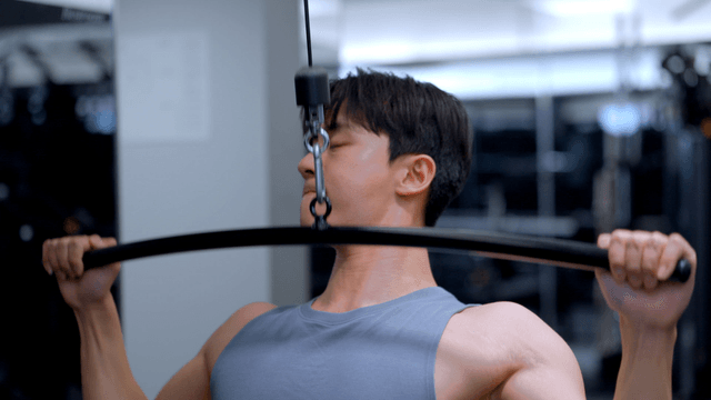 Young man training shoulders on lat pulldown machine