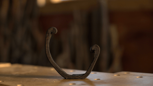 Black hook-shaped wooden sculpture on workbench