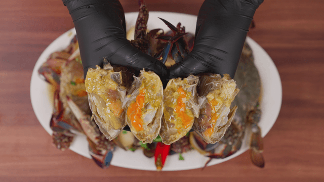 Hand holding a plate of soy sauce marinated crab with halved pieces