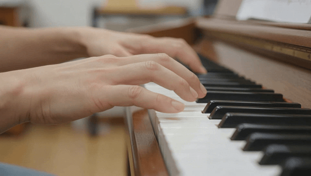Hands playing piano keys indoors