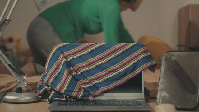 Woman tidying up bedding with a laptop covered by striped cloth
