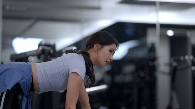 Side view of a young woman doing dumbbell rows