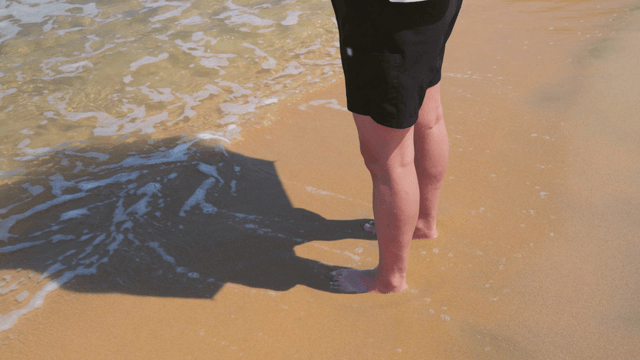 Person standing on sandy beach as waves approach