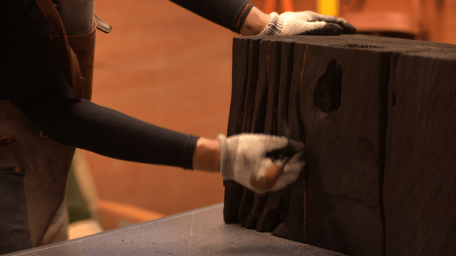 Artisan carving a dark wooden sculpture with an awl
