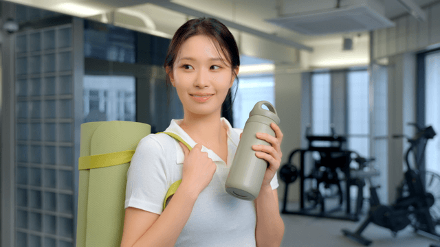 Woman smiling with a yoga mat and bottle in a gym