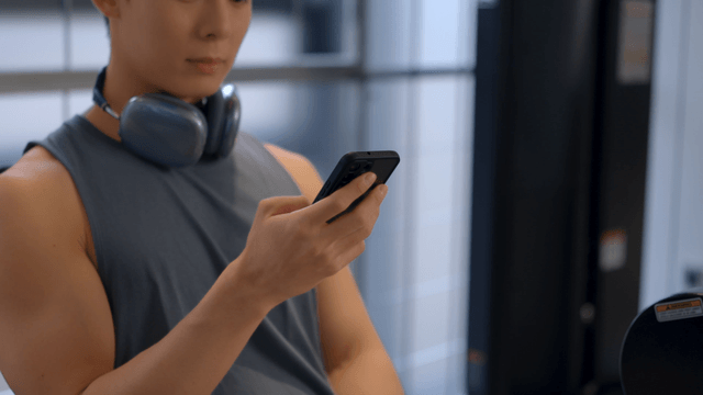 Man using smartphone with headset around neck at gym