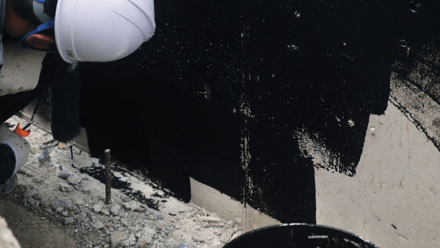Worker painting a wall with black paint
