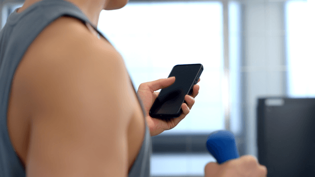 Man using smartphone while lifting a small dumbbell at gym