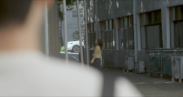 Woman standing outside building seen over man’s back