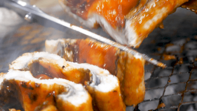 Gloved hands with scissors holding seasoned eels