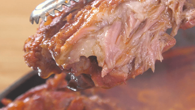 Tongs holding juicy pork back-bone meat from outer leaves stew