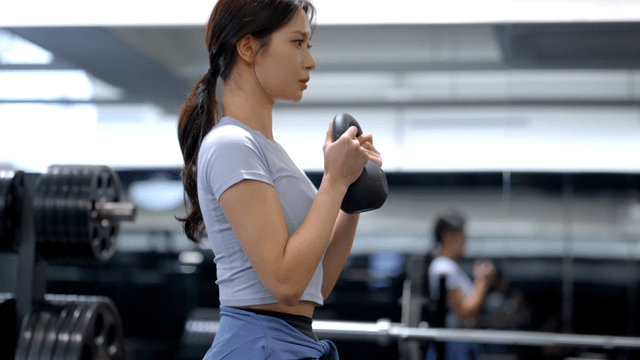 Side view of young woman doing kettlebell squats