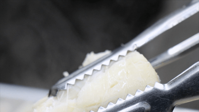 Cooked cod soup piece held with tongs