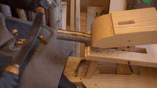 Craftsman trimming wooden branch with drawknife in workshop