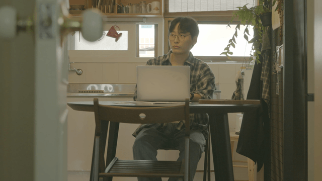 Man stands up from working on his laptop in a cozy kitchen