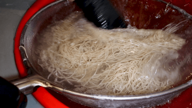Hands quickly rinsing buckwheat noodles in cold water