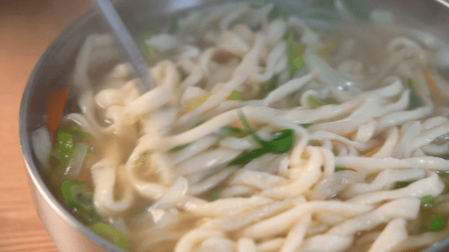 Chopsticks stirring steaming hand-cut noodles