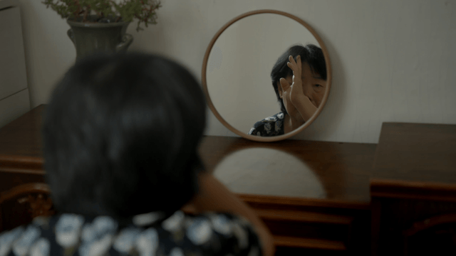 An elderly woman adjusting hair in front of a mirror